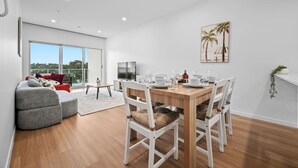 A modern living room with a dining area, large windows, and a flat-screen TV.