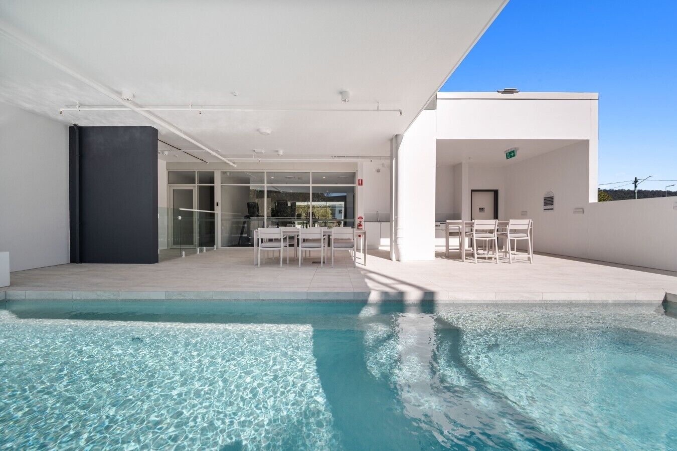Zona de piscina exterior moderna amb aigua cristal·lina, zona de seients amb cadires i espai tancat amb vidre.