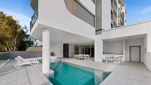 A modern building with a swimming pool, outdoor seating, and a covered patio area.