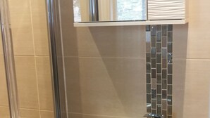 Een badkamer met een douchecabine van glas, een witte wastafel met kraan en een spiegel erboven.