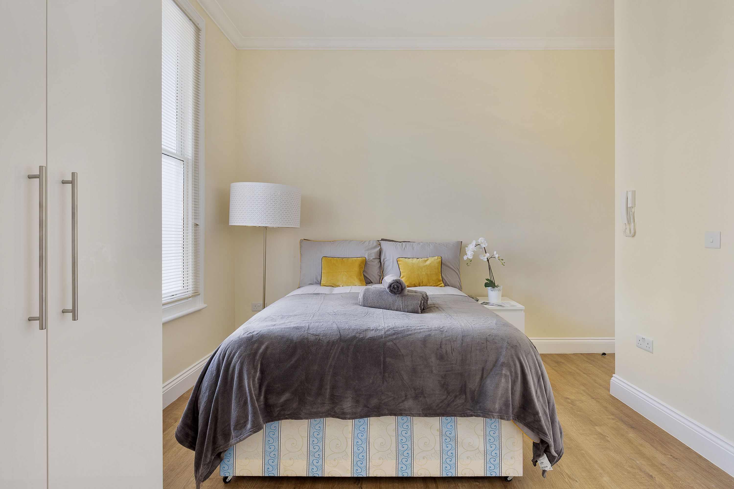 Ein Schlafzimmer mit Bett, Nachttisch, Lampe und Fenster.