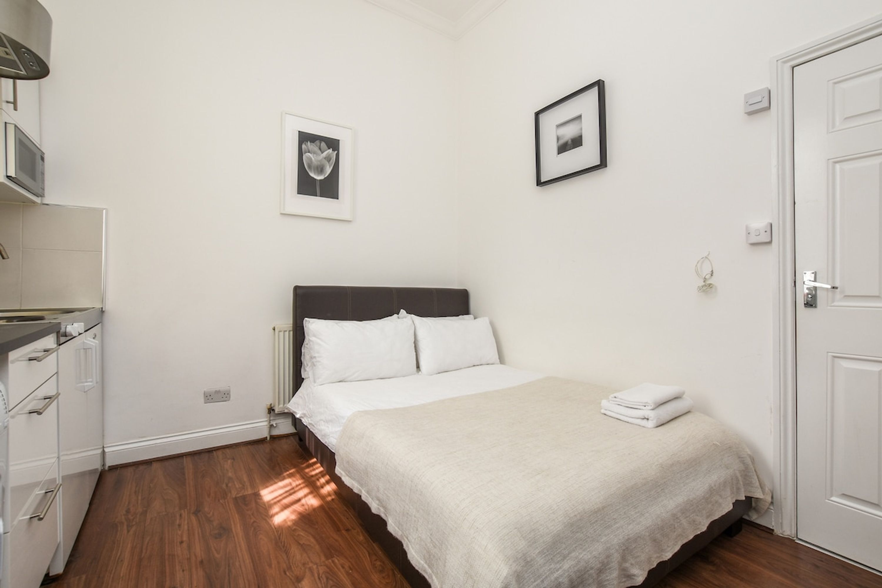 A bedroom with a bed, a dresser, a microwave, and a door.
