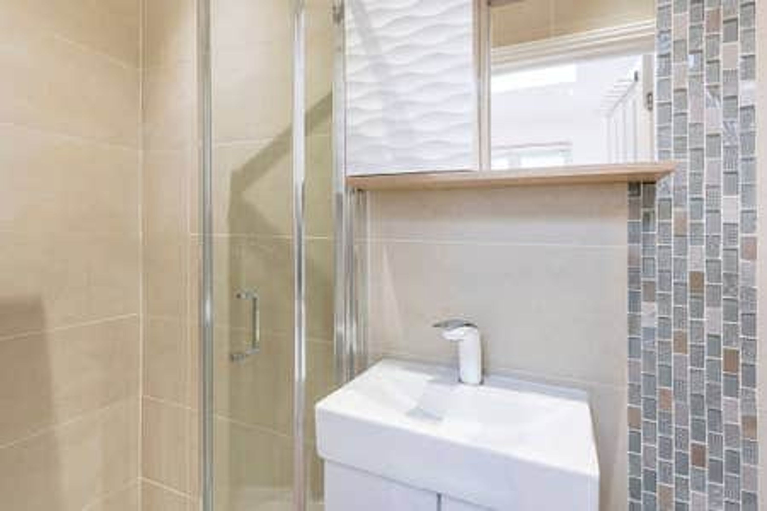 A bathroom with a glass shower enclosure, a white sink, and a tiled backsplash.