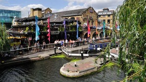 A riverside walkway with a bridge, buildings, and flags. - Spacious Studio Flat - Camden Kings Cross Zone 1 (London)