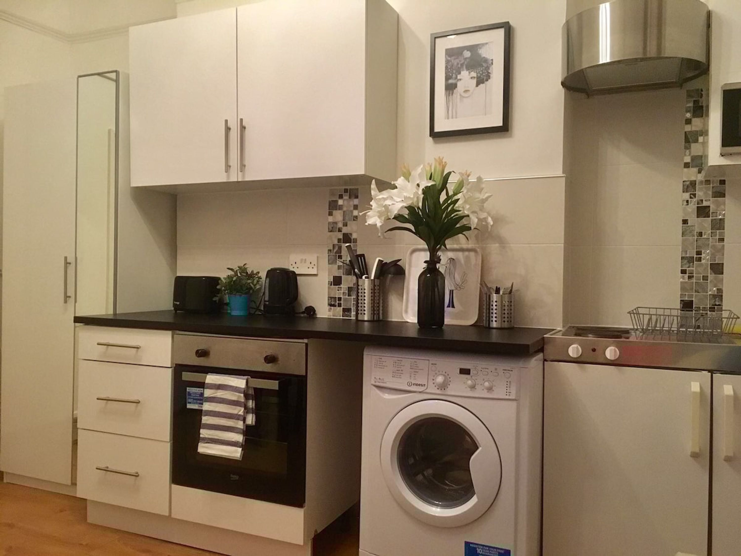 Cocina compacta con armarios blancos, horno integrado, lavadora y microondas.