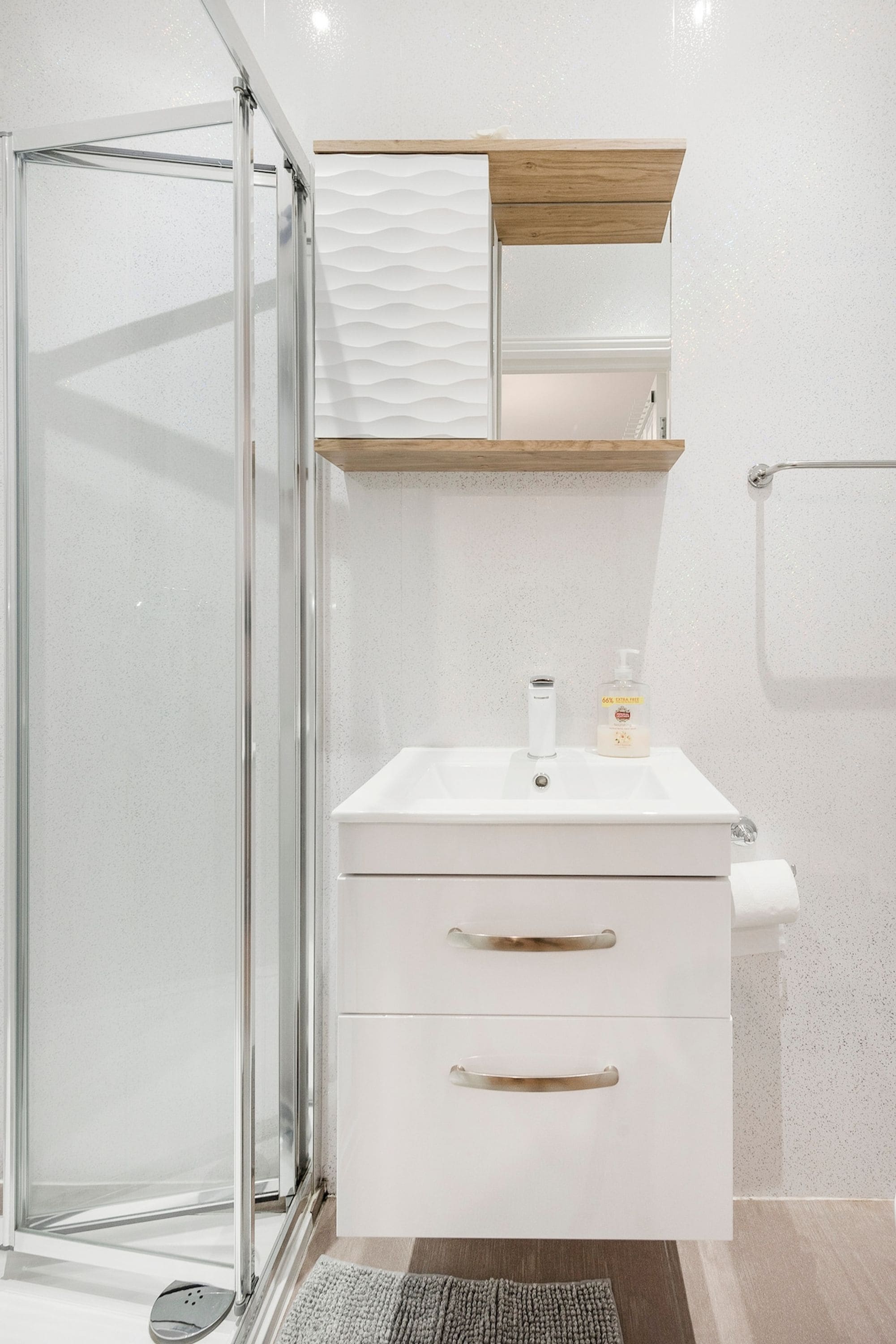 A bathroom with a glass shower enclosure, a white sink with a soap dispenser, and a towel rack.
