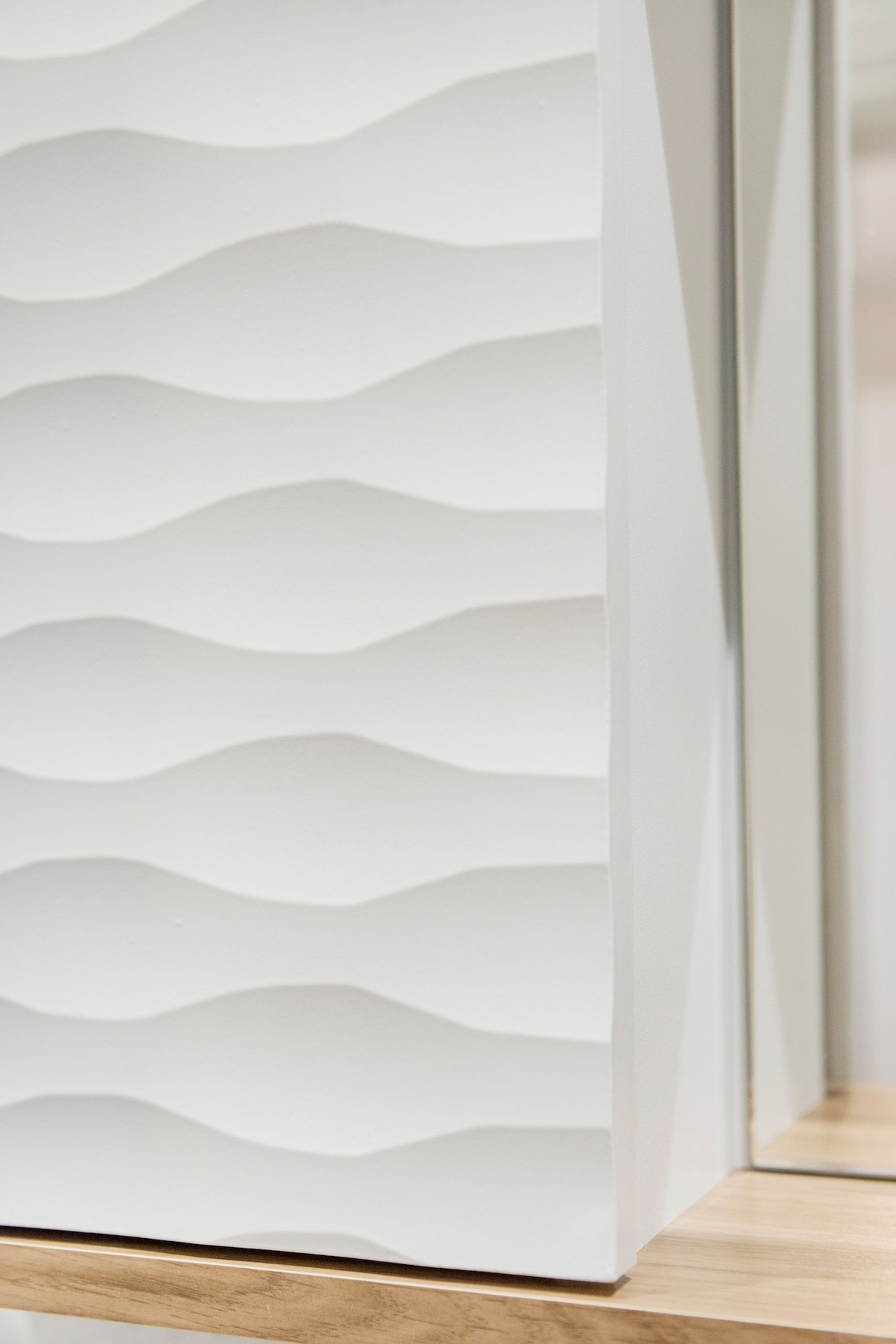 A white, wavy-textured wall with a wooden baseboard.
