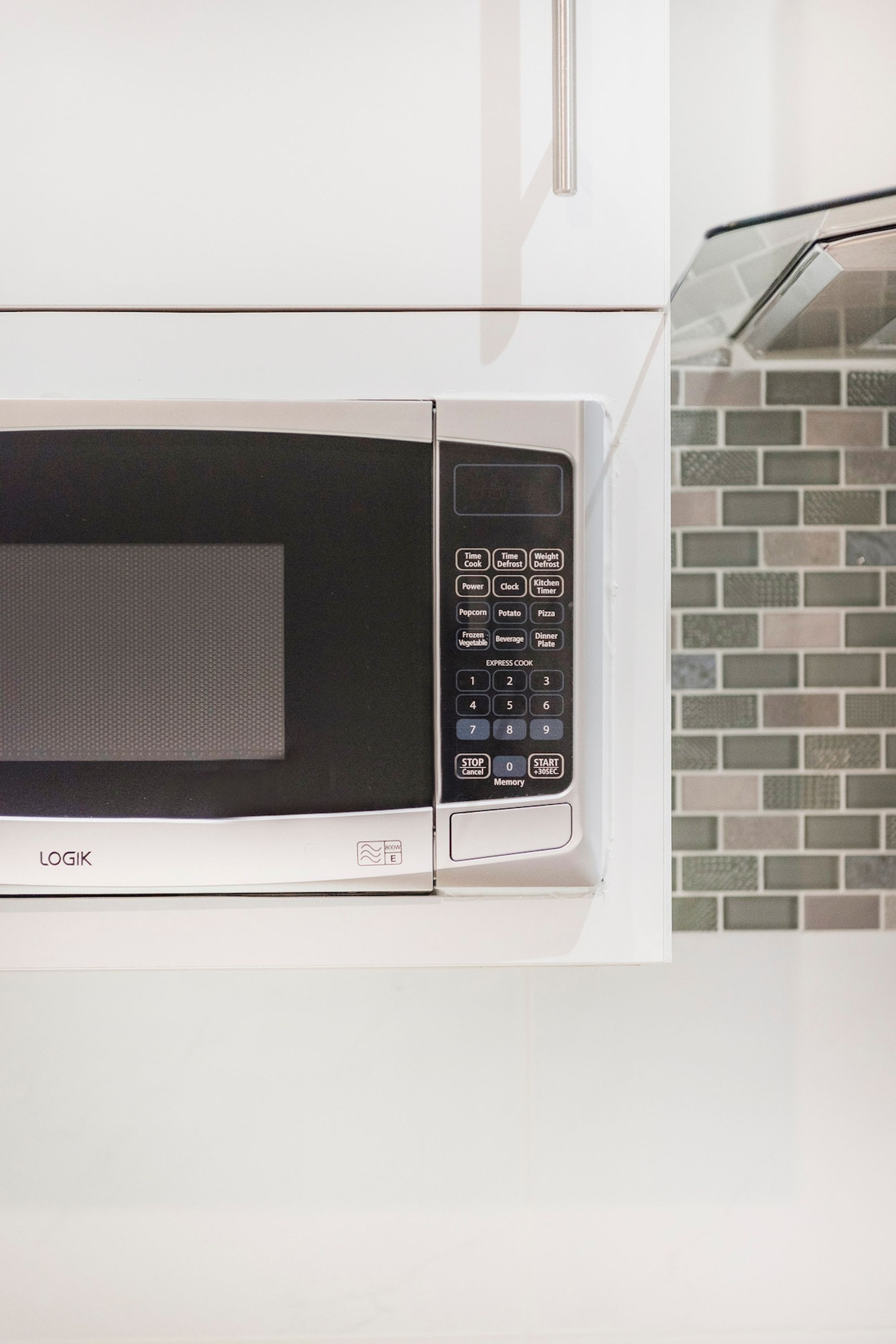 A microwave oven with a digital control panel, brand name 'LOGIK,' and a 'START/STOP' button.
