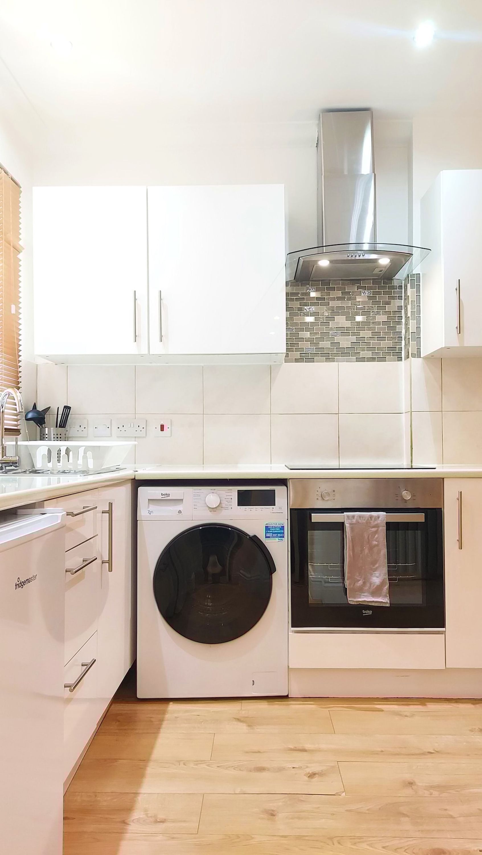 A compact kitchen with a washing machine, oven, and a glass-fronted range hood.