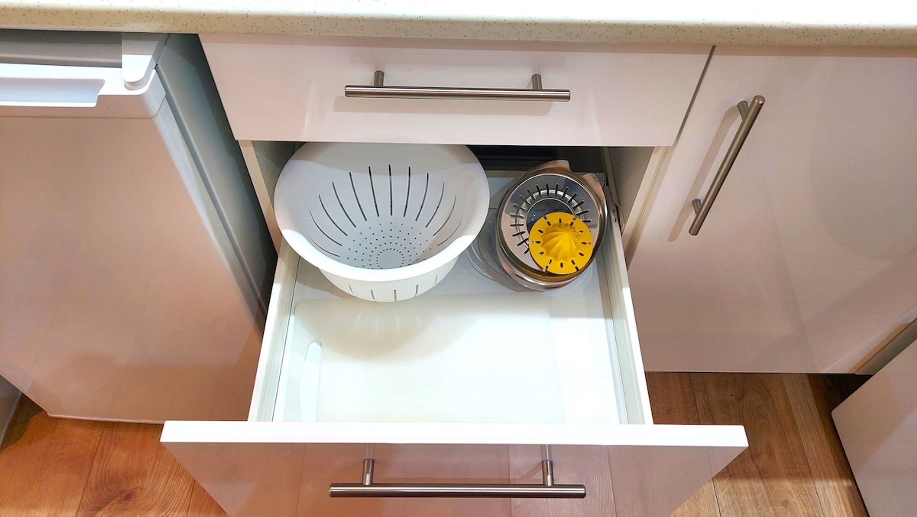 A kitchen drawer with a colander, a yellow kitchen timer, and a white colander.