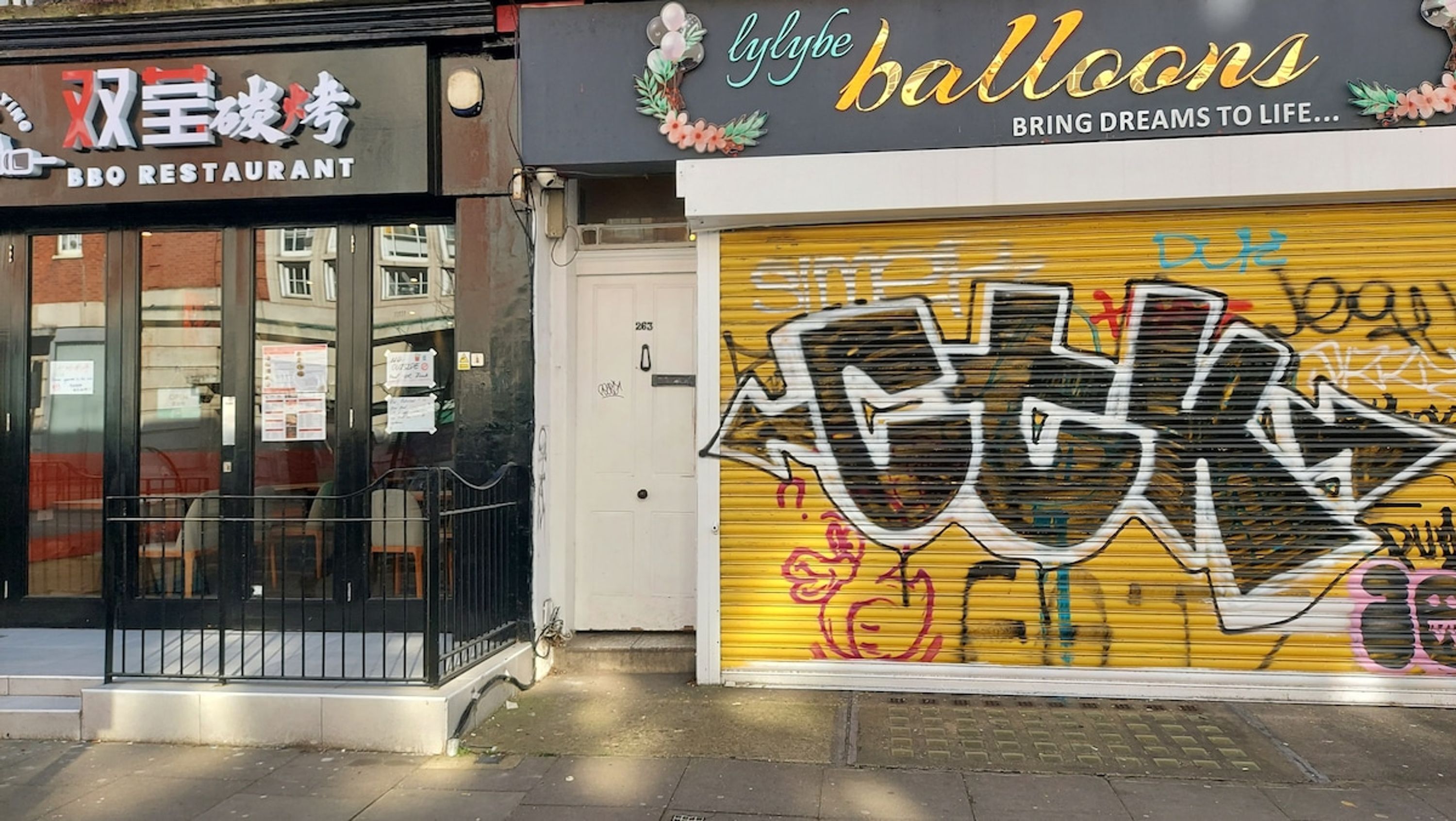 A storefront with a closed yellow shutter, graffiti, and a sign for 'balloons' above.