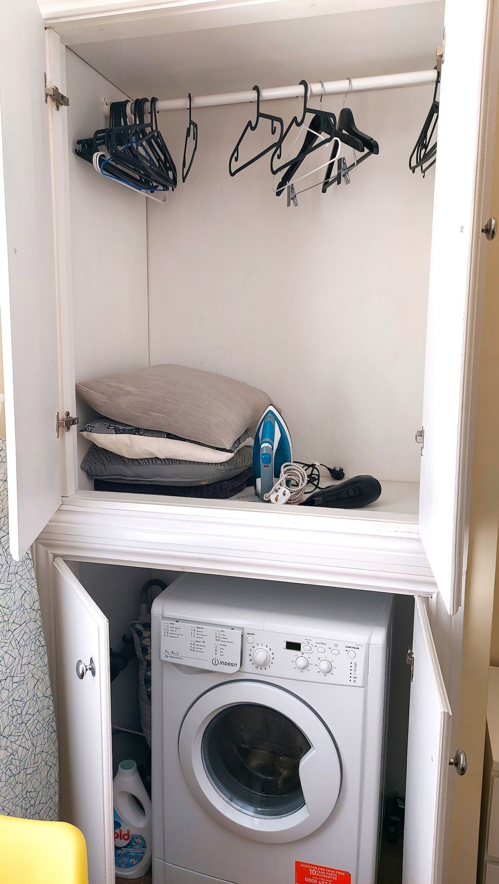 A laundry room with a washing machine, ironing board, and hanging clothes.