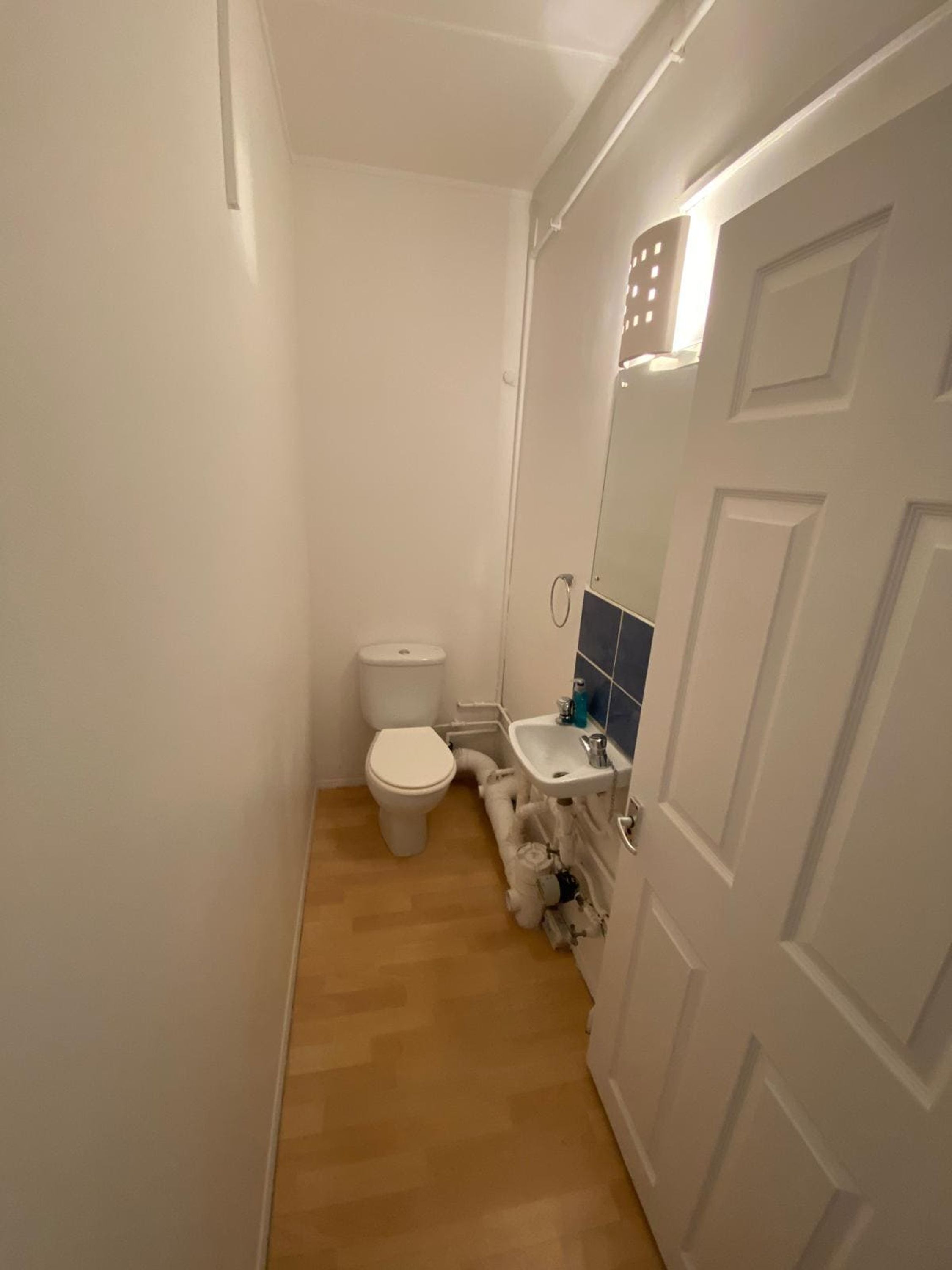 A narrow bathroom with a toilet, sink, and mirror.