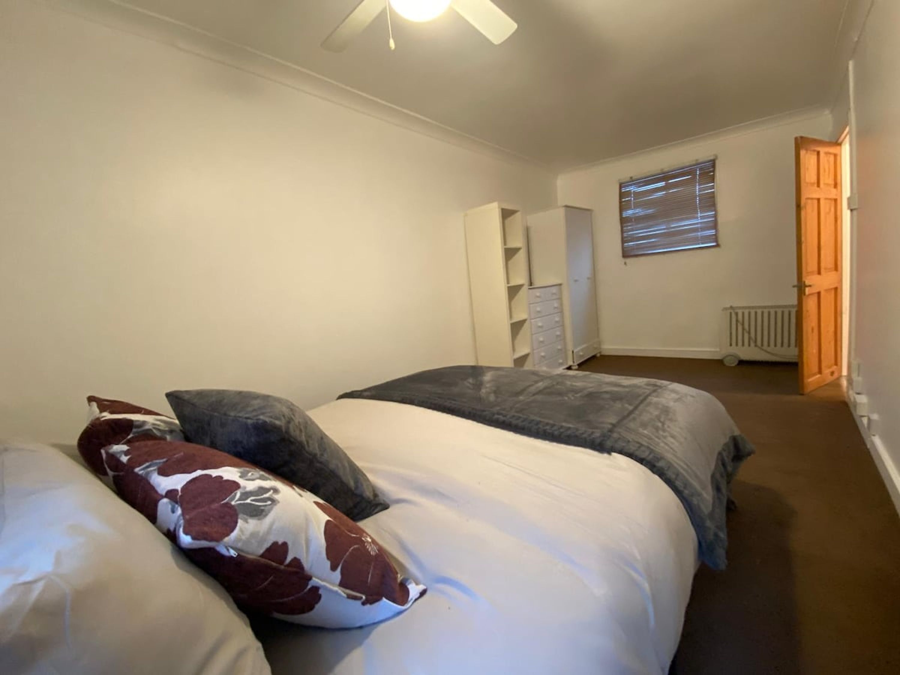 A bedroom with two beds, a wardrobe, a radiator, and a window with blinds.
