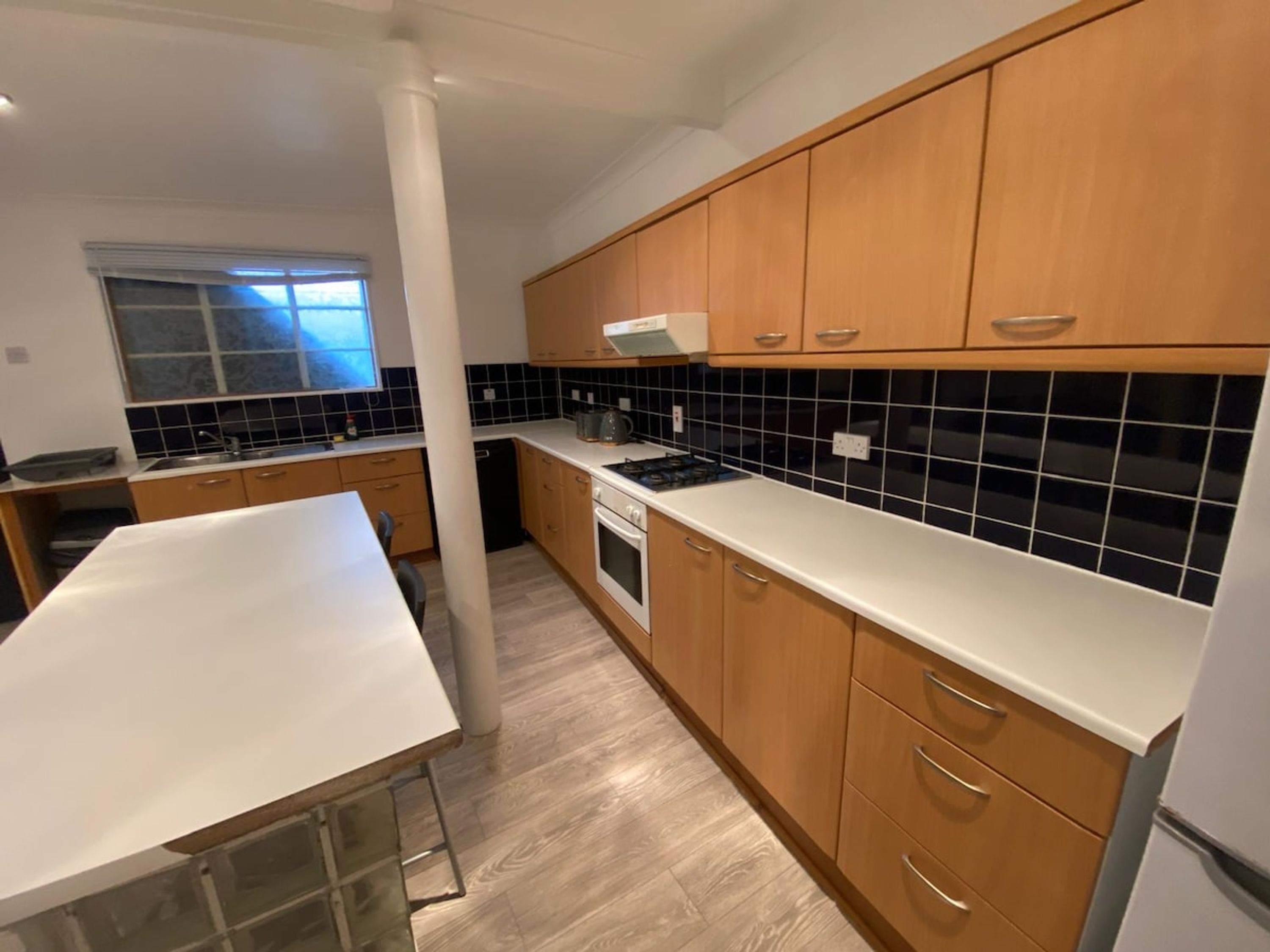 A modern kitchen with wooden cabinets, a white countertop, and a tiled backsplash.