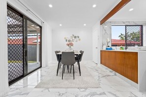 A modern kitchen with a marble countertop, a dining area with a table and chairs, and a view through a sliding door. - Value Family-Friendly Stay | Near Shops & Dining (Sunnybank Hills)