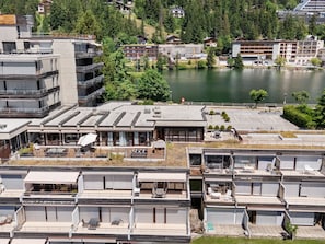 Ein modernes Hotel mit mehreren Etagen, Sitzgelegenheiten im Freien und Blick auf einen See.