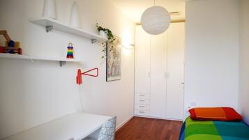 Ein Schlafzimmer mit Bett, Schreibtisch, Kleiderschrank und Regalen mit Gegenständen.
