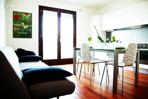 Una sala de estar moderna con un sofá, comedor con sillas, una cocina y una puerta que da al exterior.