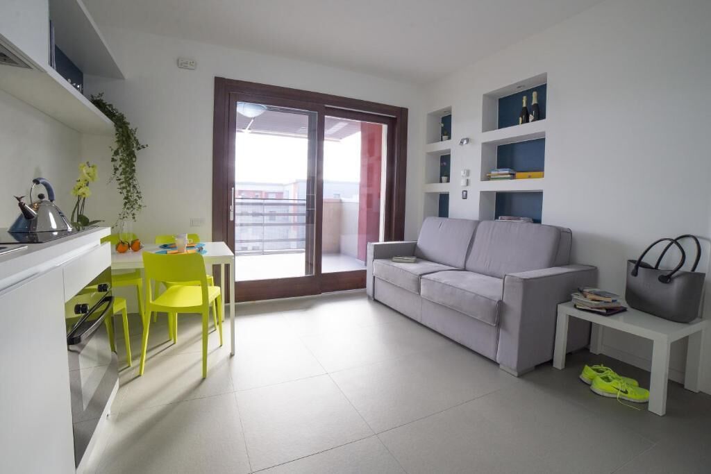 A modern apartment with a dining area, a sofa, a small table, a balcony, and a kitchen area.