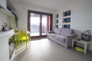 En moderne lejlighed med spiseplads, sofa, lille bord, balkon og et køkkenområde.