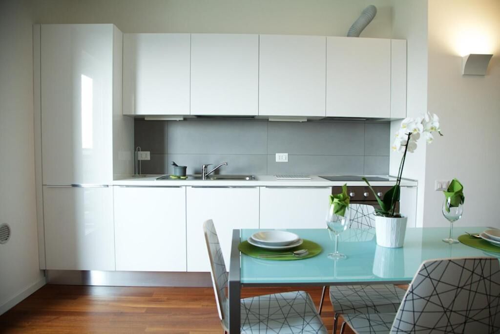 Una cocina moderna con armarios blancos, una mesa de comedor con sillas y una orquídea en maceta sobre la mesa.