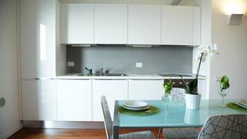 Una cocina moderna con armarios blancos, una mesa de comedor con sillas y una orquídea en maceta sobre la mesa.
