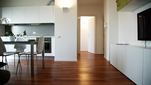 Una cocina moderna con armarios blancos, una zona de comedor con sillas y piso de madera.