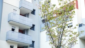 Un edificio de varios pisos con balcones y un árbol en frente.