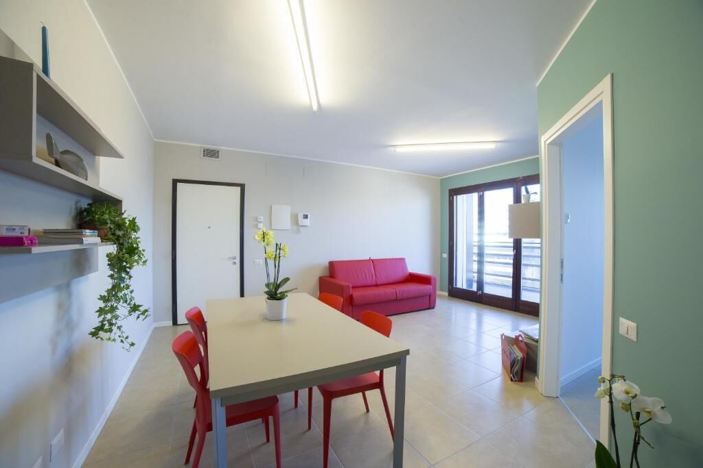 A modern living room with a dining table, red chairs, a red sofa, and a large window.