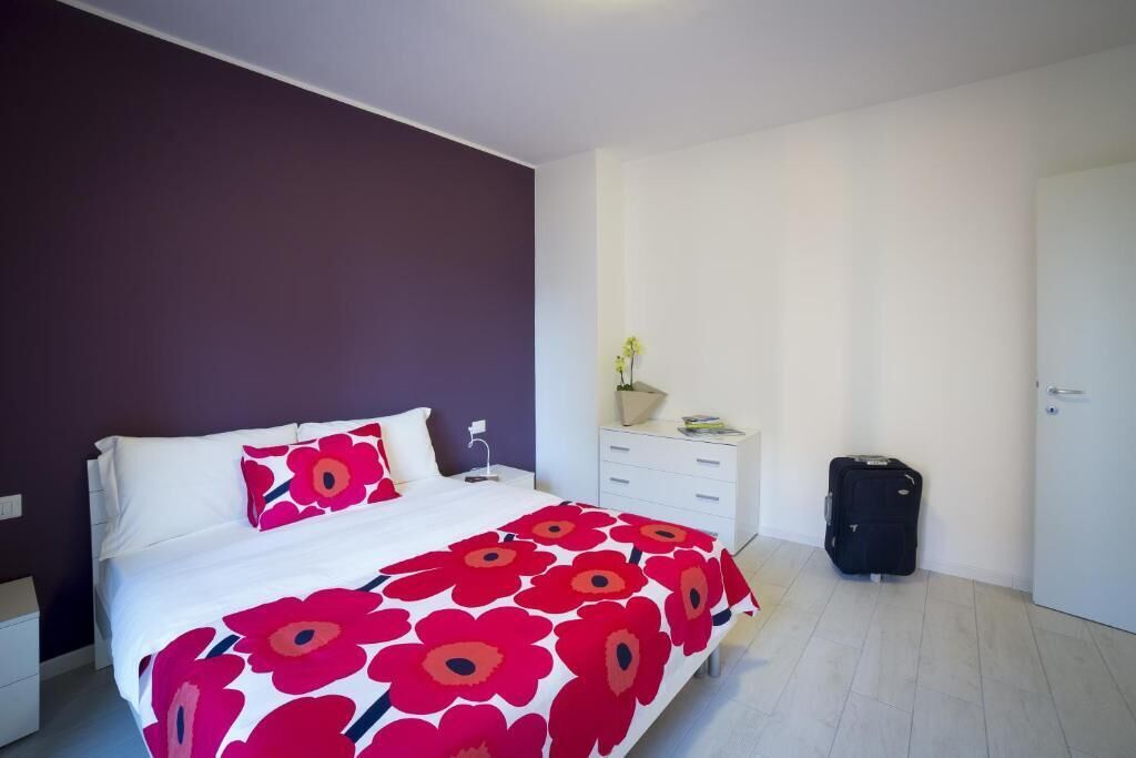 Un dormitorio con cama, mesita de noche, cómoda, maleta y puerta.