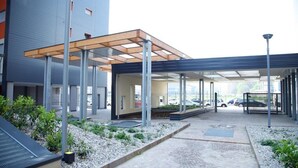 Un espacio al aire libre techado con un edificio moderno, un sendero pavimentado y un estacionamiento.