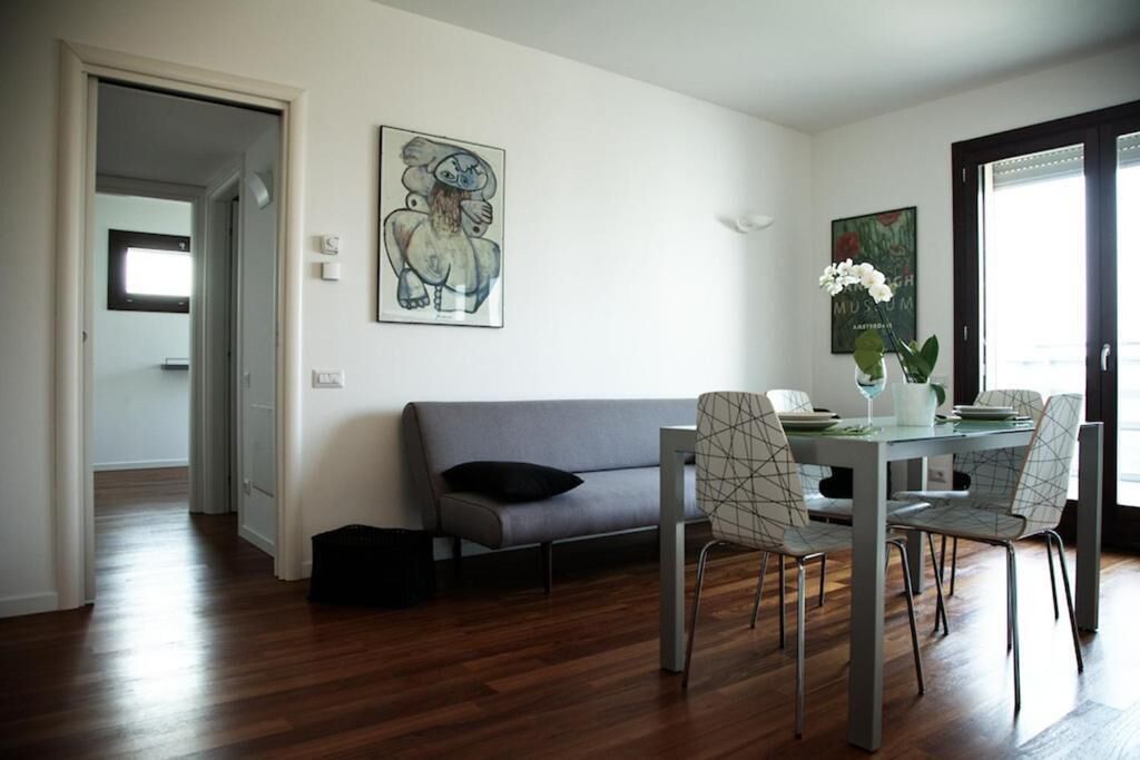 Una sala moderna con un sofá gris, mesa de comedor con sillas y obras de arte en las paredes.