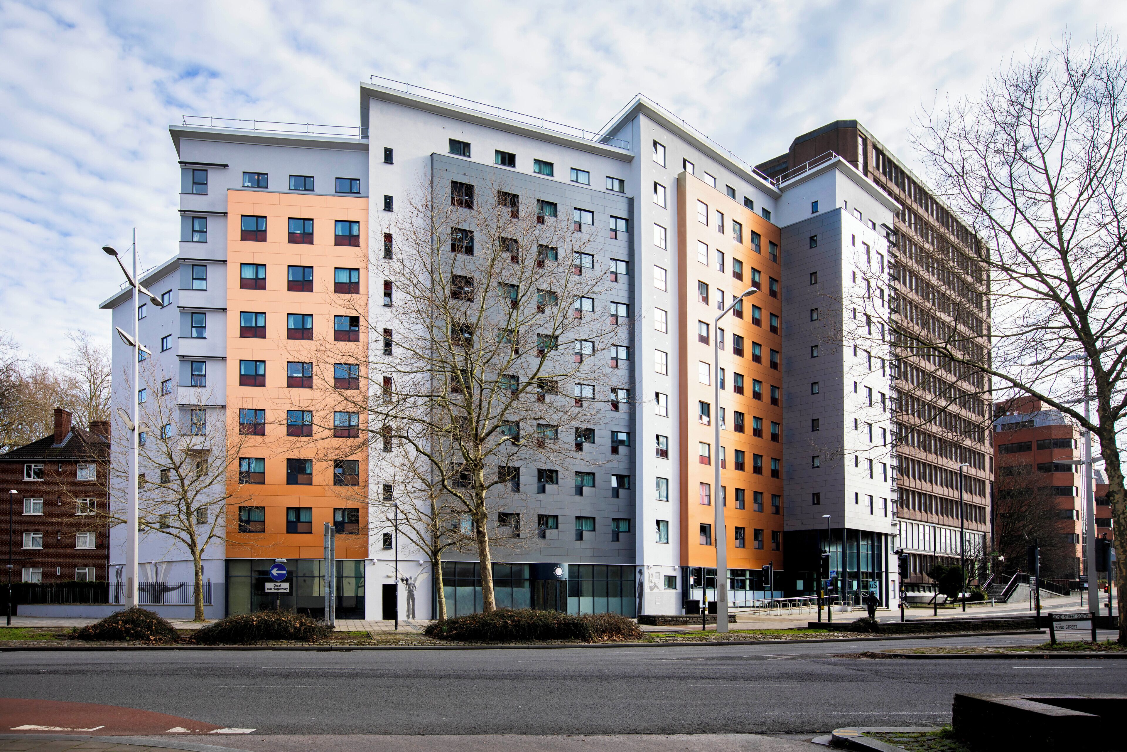 Un edificio de varios pisos con un diseño arquitectónico moderno, que combina diferentes estilos de ventanas y materiales de construcción.