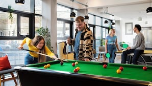 A pool table in a room with large windows, chairs, and hanging lights. - Student Only Phoenix Court (Bristol)