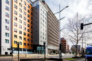 Un immeuble à plusieurs étages, doté d’un style architectural moderne, avec une façade combinant verre et brique, et une entrée bien visible avec une porte en verre.