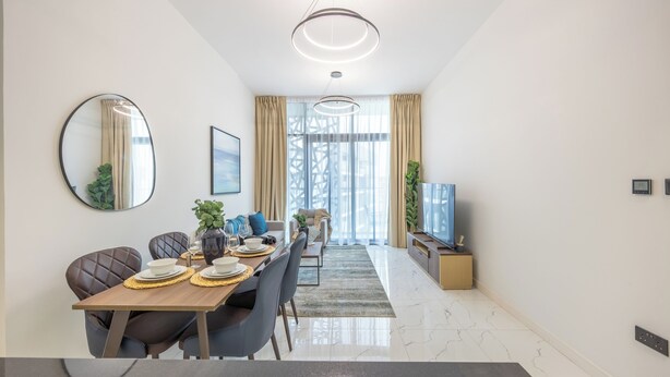 A modern dining area with a long table, chairs, and a television on a stand. - Bloomfields 2BR in The Gate - Masdar  (Abu Dhabi)