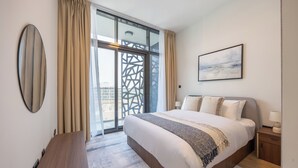 A modern hotel room with a large bed, a wooden nightstand, a round mirror, and a view through a large window. - Bloomfields 2BR in The Gate - Masdar  (Abu Dhabi)