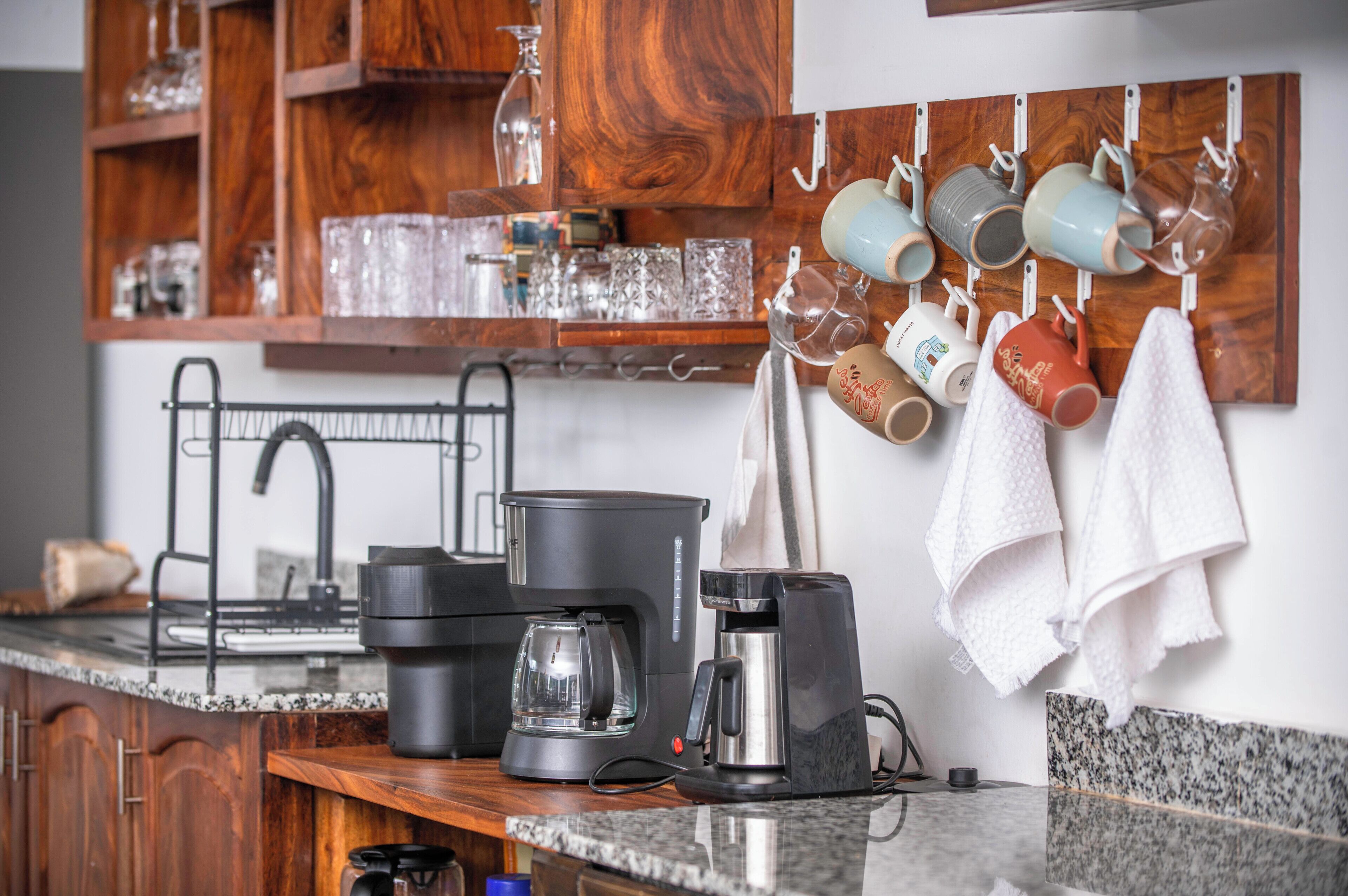 A kitchen with a coffee maker, a kettle, and a hanging mug rack.