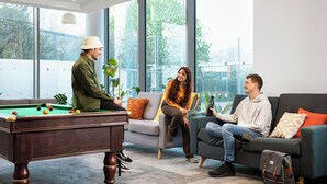 A pool table in a room with large windows, a sofa, and a couch. - Unite Students - North Lodge - London (London)