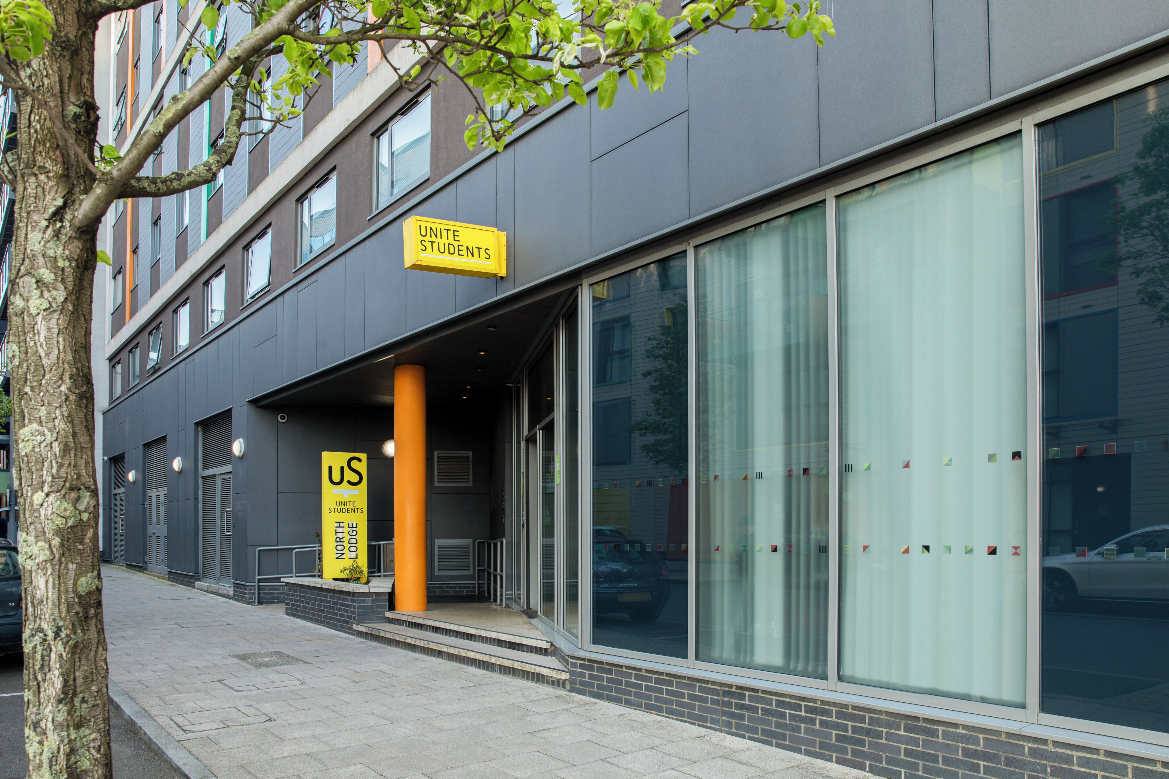 A building with a 'UNITED STUDENTS' sign, large windows, and a tree in front.