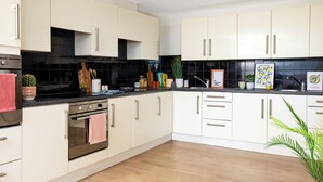 A modern kitchen with white cabinets, a black backsplash, and a wooden floor. - Unite Students - North Lodge - London (London)