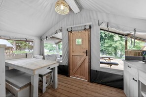 Una carpa con una mesa de madera, asientos tipo banco, una puerta y vistas al exterior.