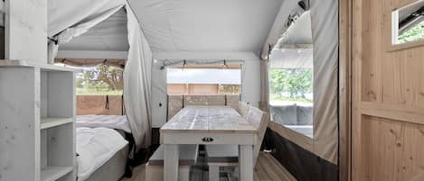 A tent with a table and benches, wooden flooring, and a window.