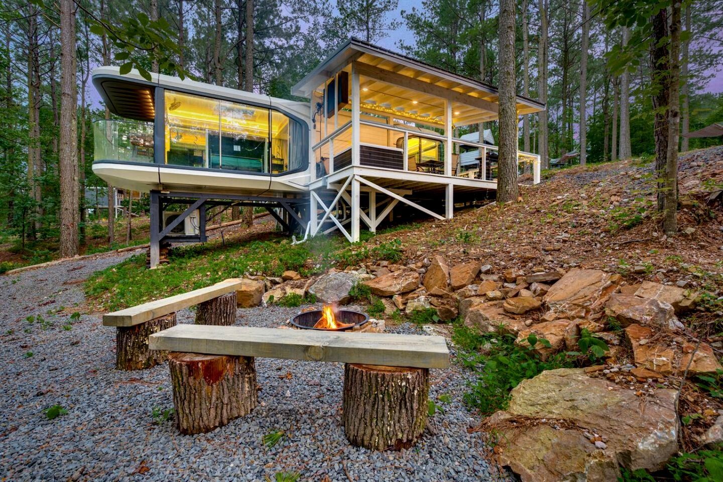 A modern cabin with a glass enclosure, a deck, and a fire pit.