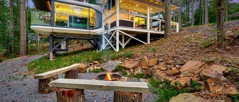 A modern cabin with a glass enclosure, a deck, and a fire pit.