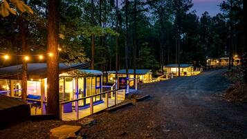 A rustic cabin-style hotel with multiple rooms, a covered outdoor seating area, and a dirt path leading through the forest.