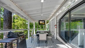Une terrasse extérieure couverte, équipée d’un barbecue, de tables, de chaises et d’un écran de télévision.