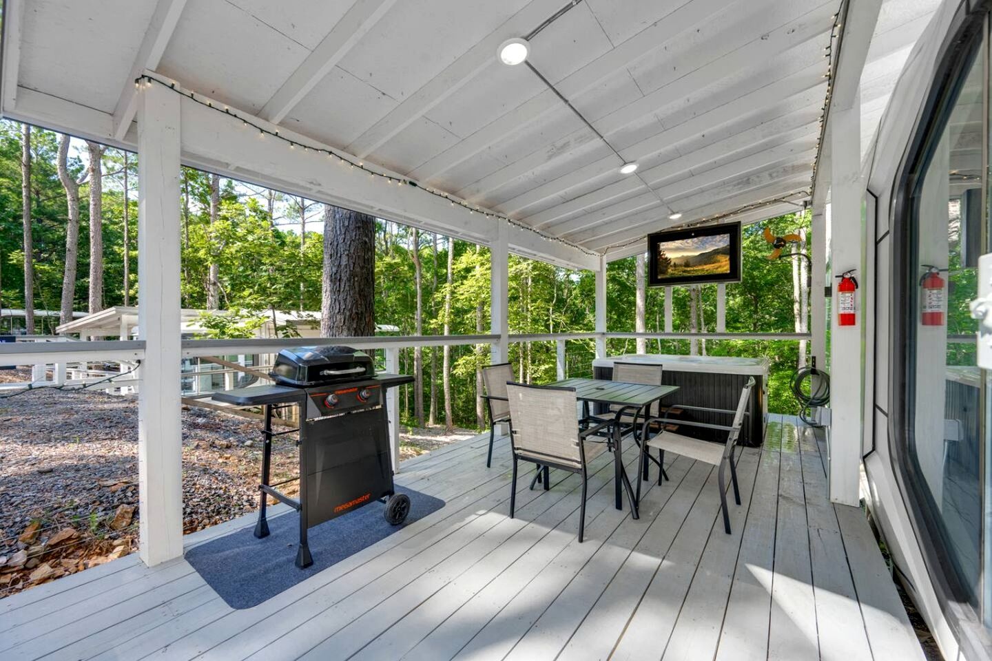 A covered outdoor patio with a grill, seating area, and a TV screen.
