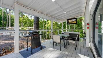 A covered outdoor patio with a grill, seating area, and a TV screen.